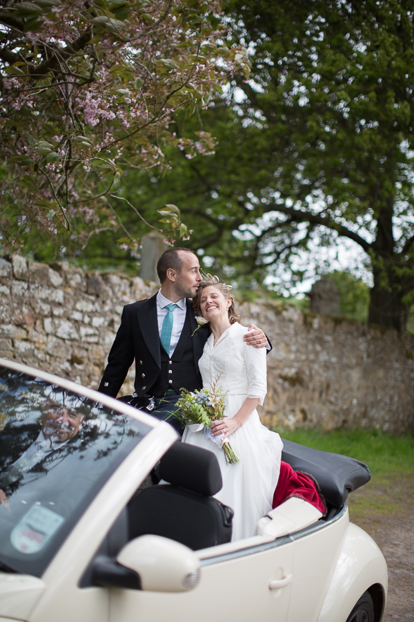 bride and groom huging driving away in a car