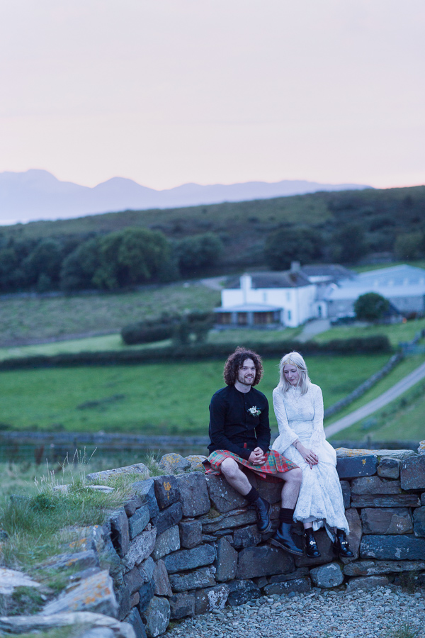 bride and groom sitting an a brick wall with view