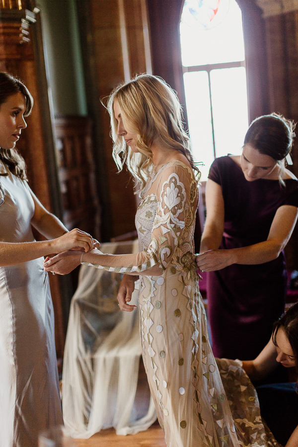 bride putting dress on bridesmates helping
